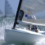 A small sail boat blasting through a wave during a race.